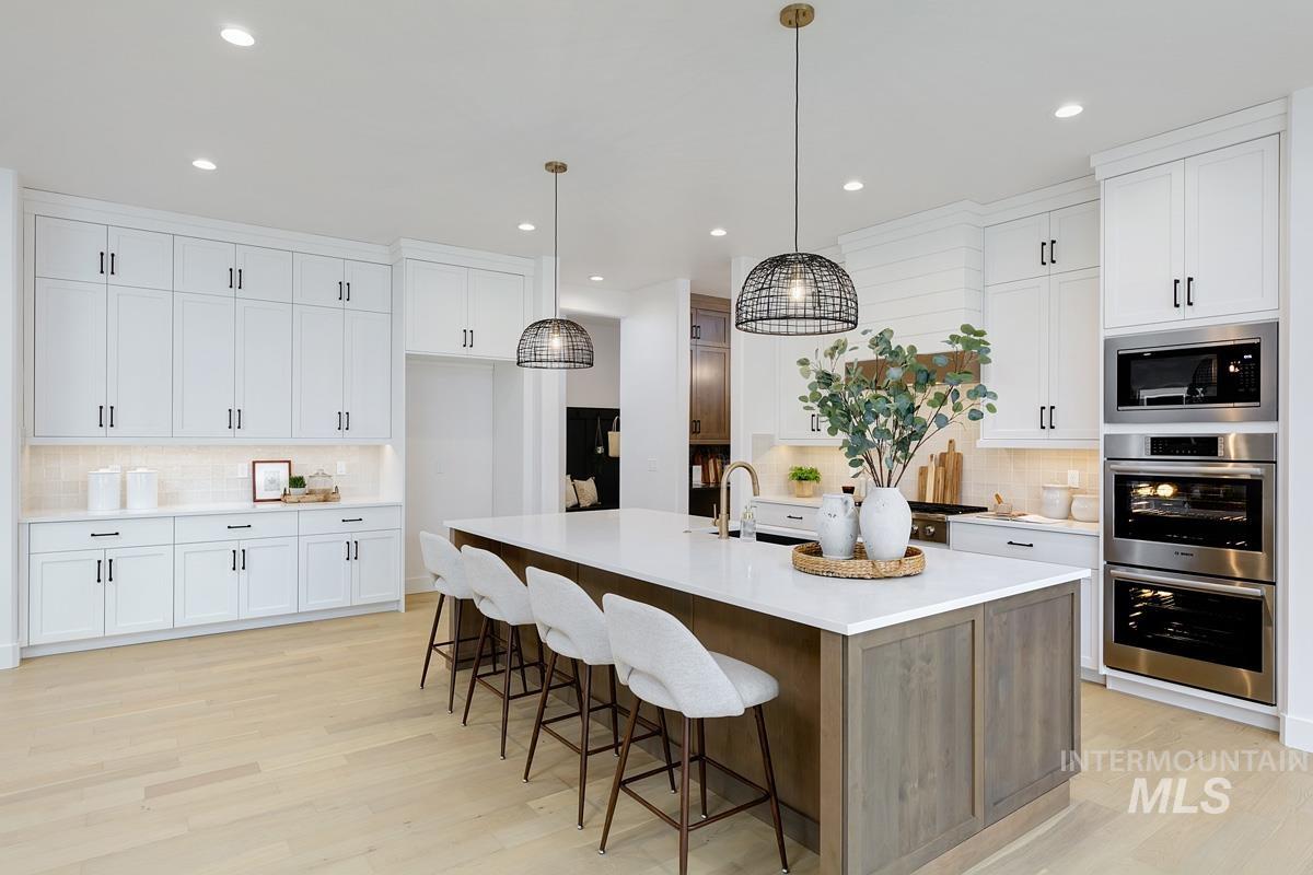 13624 North Ruffed Grouse Way Boise, ID 83714 - Photo 3 of 41 Kitchen featuring tasteful backsplash, light wood finished floors, white cabinetry, a kitchen island with sink, and recessed lighting