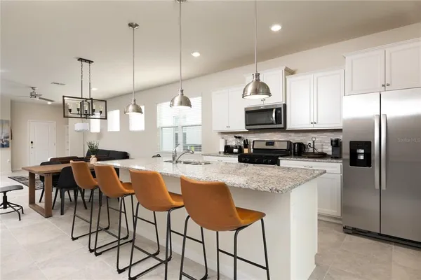 a kitchen with stainless steel appliances granite countertop a sink a stove a refrigerator cabinets and chairs