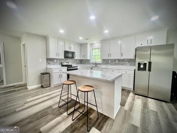 a kitchen with stainless steel appliances granite countertop a stove a sink a refrigerator and white cabinets with wooden floor