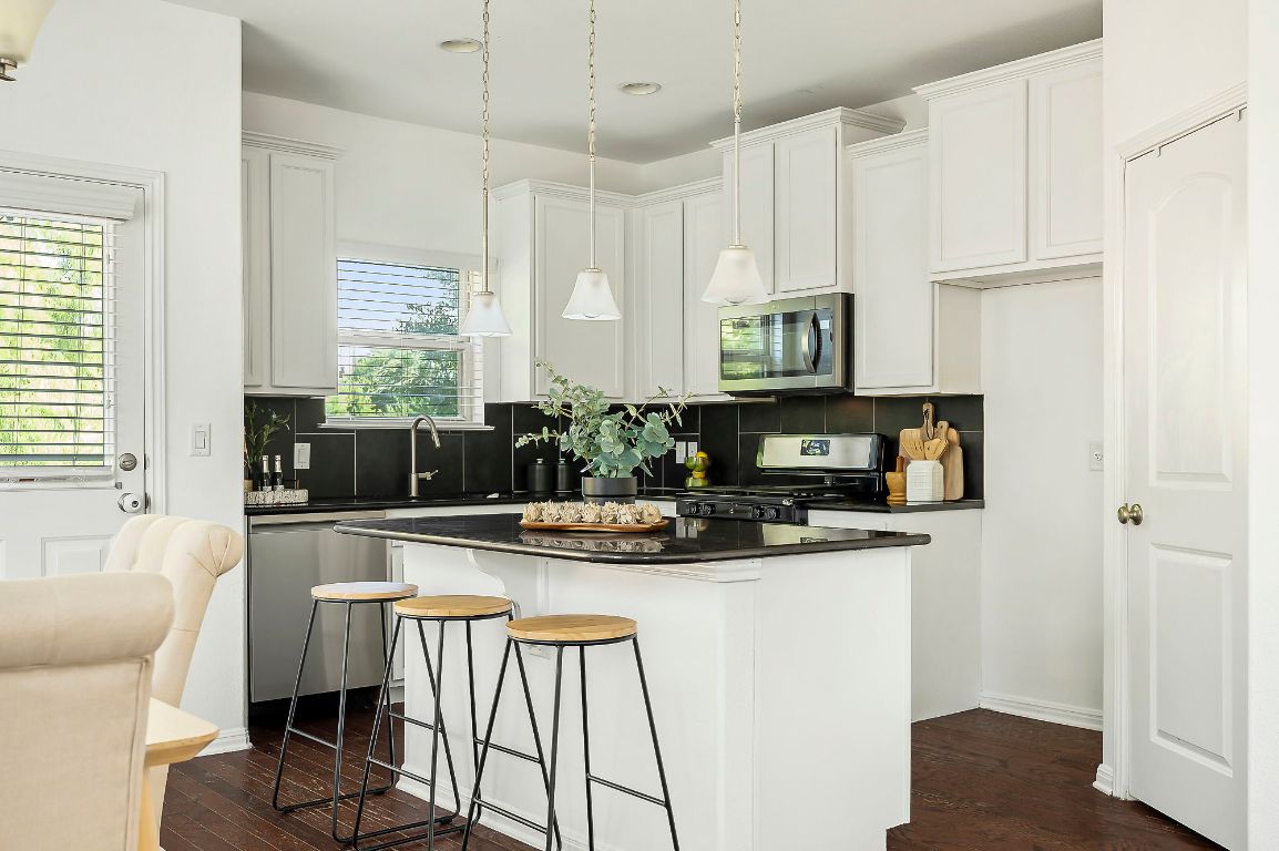 800 Totis Road Austin, TX 78748 - Photo 10 of 29 Kitchen featuring a center island, a kitchen bar, dark wood-type flooring, stainless steel appliances, and decorative light fixtures