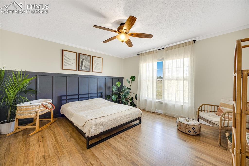 17520 Fremont Fort Road Peyton, CO 80831 - Photo 21 of 42 This bedroom features hardwood floors, a prominent paneled accent wall, and a ceiling fan with integrated lighting