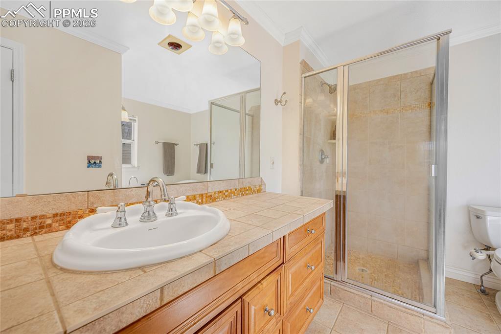 17520 Fremont Fort Road Peyton, CO 80831 - Photo 23 of 42 The bathroom features a tiled vanity with a white sink and chrome faucet, a large mirror, and a glass-enclosed shower