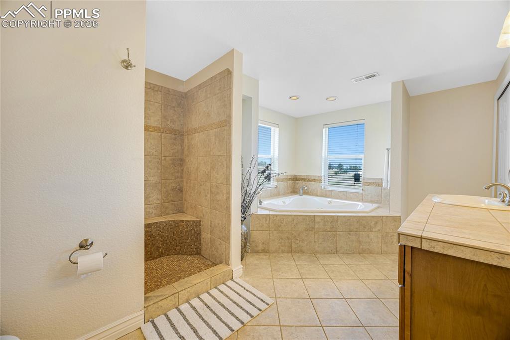 17520 Fremont Fort Road Peyton, CO 80831 - Photo 31 of 42 This bathroom features a tiled shower with a built-in bench, a spacious corner tub with tiled surround, and a vanity with a counter and sink