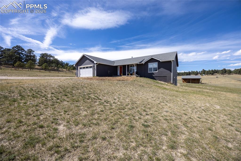 17520 Fremont Fort Road Peyton, CO 80831 - Photo 4 of 42 This property features a single-story residence with a dark exterior, a prominent garage, and a sloped gray roof, set against a backdrop of natural landscaping and a clear blue sky