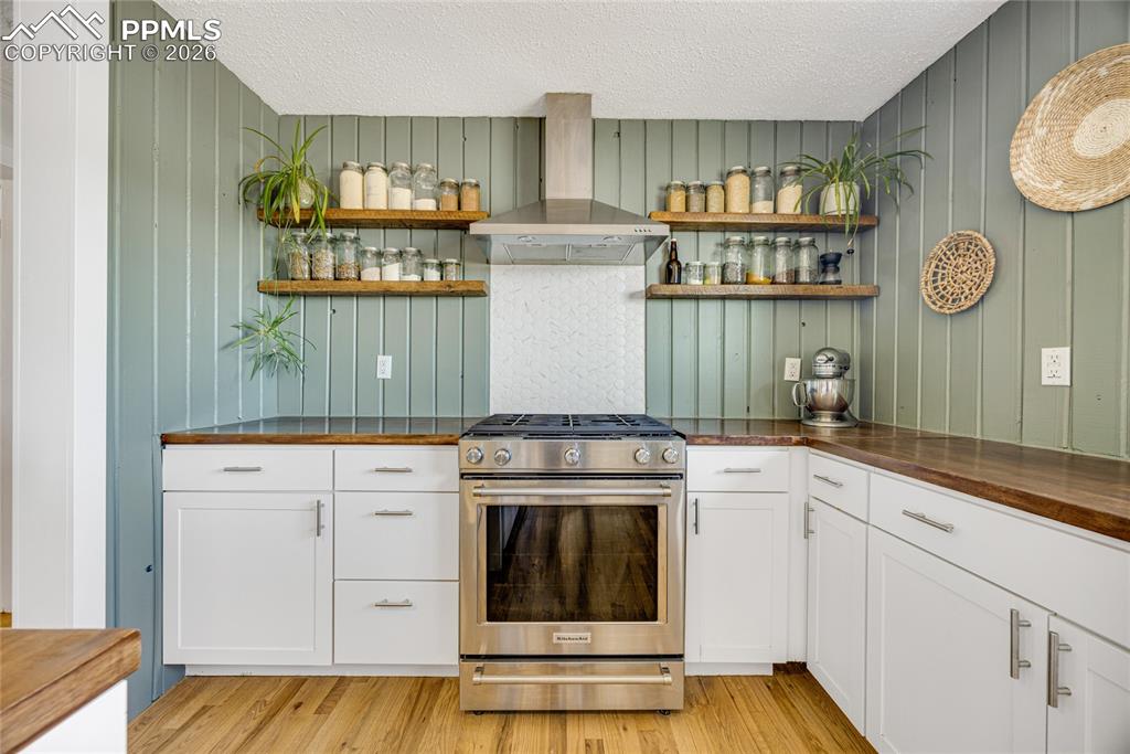 17520 Fremont Fort Road Peyton, CO 80831 - Photo 8 of 42 The kitchen features white cabinetry, wood countertops, and a stainless steel range with a matching range hood and open shelving