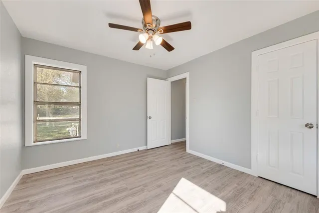 an empty room with wooden floor chandelier fan and windows