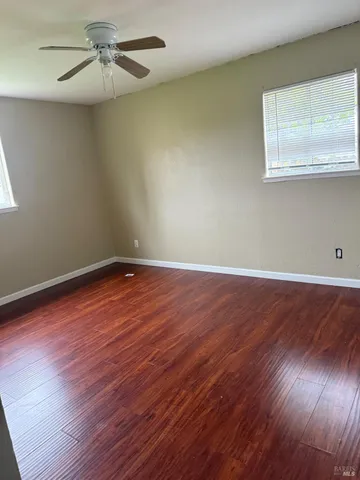 an empty room with wooden floor fan and windows