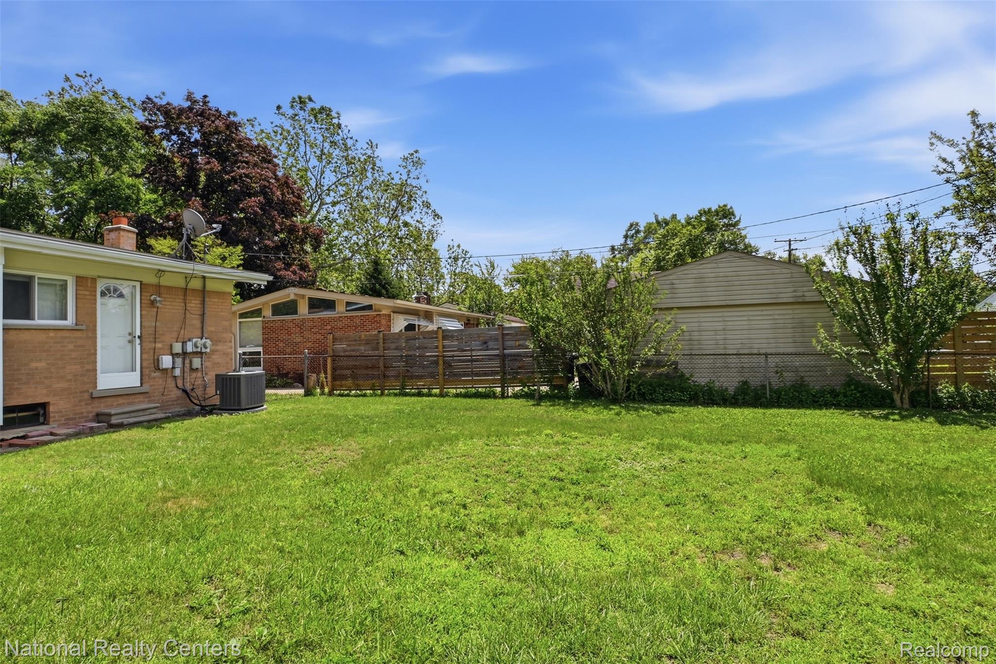 17159 Rougeway Street Livonia, MI 48152 - Photo 35 of 36 Expansive green lawn with a partial brick exterior, white rear entry door, and central air conditioning unit