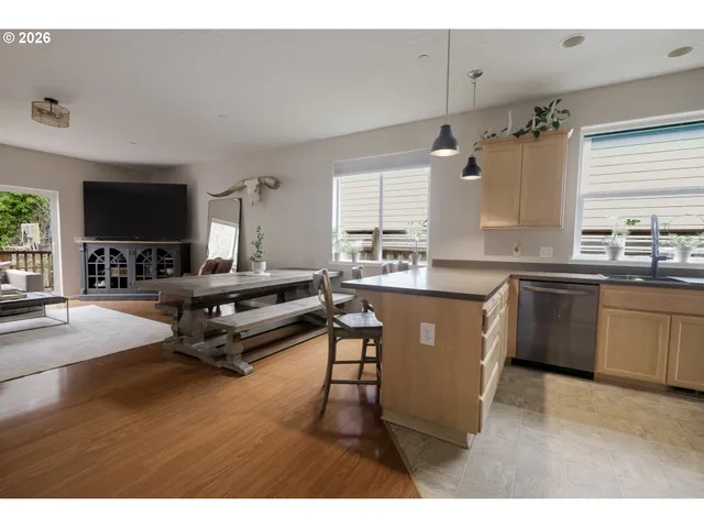 a living room with stainless steel appliances kitchen island granite countertop a sink dishwasher a stove and a dining table with wooden floor