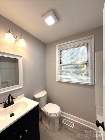 a bathroom with a toilet a sink a mirror a window and vanity