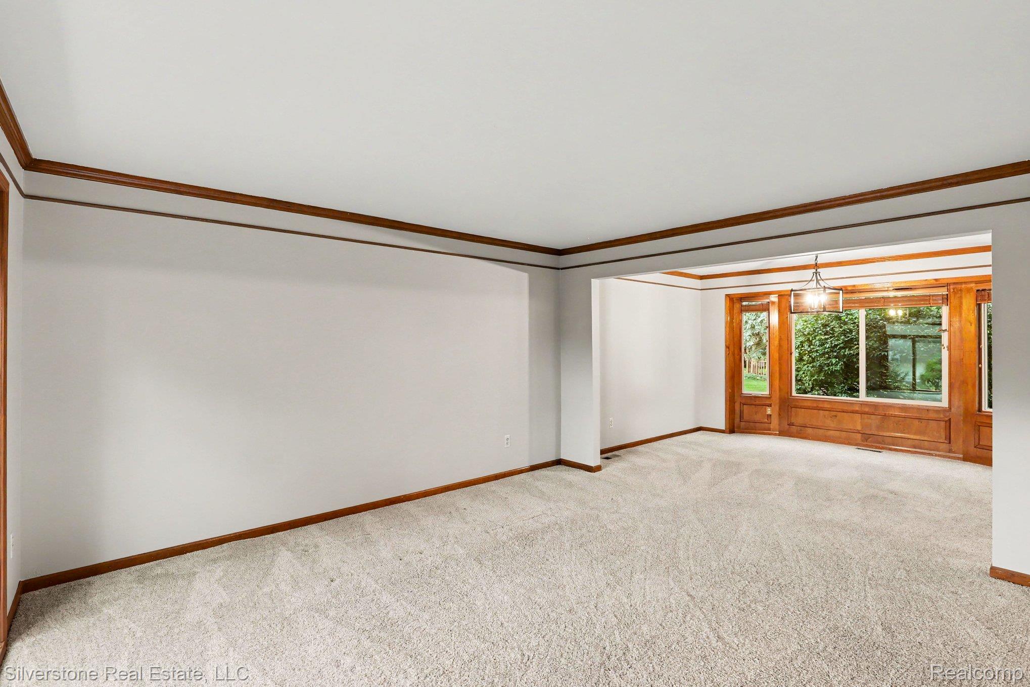 869 Timberline Drive Rochester, MI 48309 - Photo 8 of 29 Light-toned carpet flooring, white walls, wood trim detailing, and an open entryway to an additional space featuring large windows