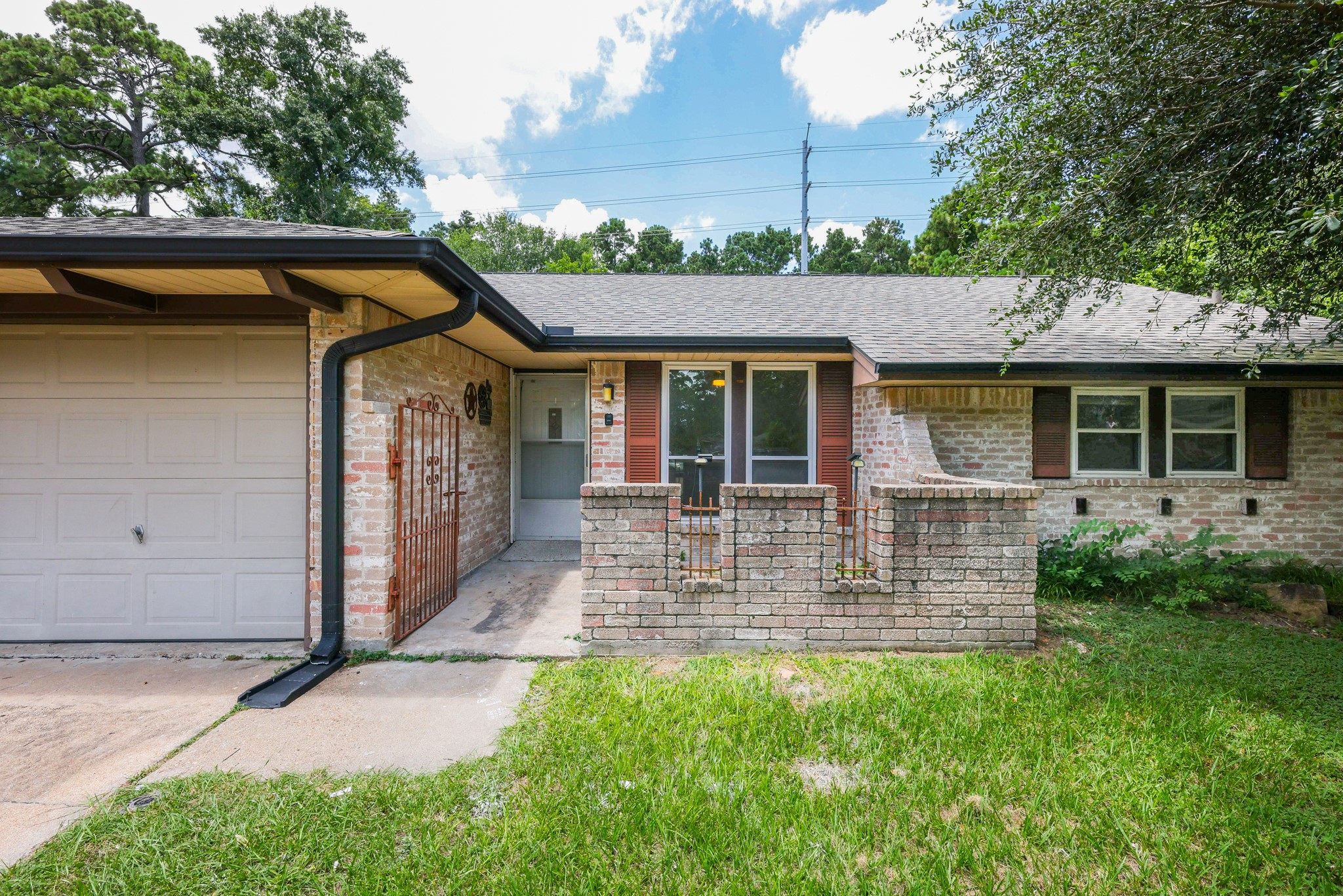 4823 Connorvale Road Houston, TX 77039 - Photo 2 of 26 Charming single-story home features a brick exterior with a covered front entryway, attached garage, and a small front patio. It's surrounded by lush greenery and mature trees.