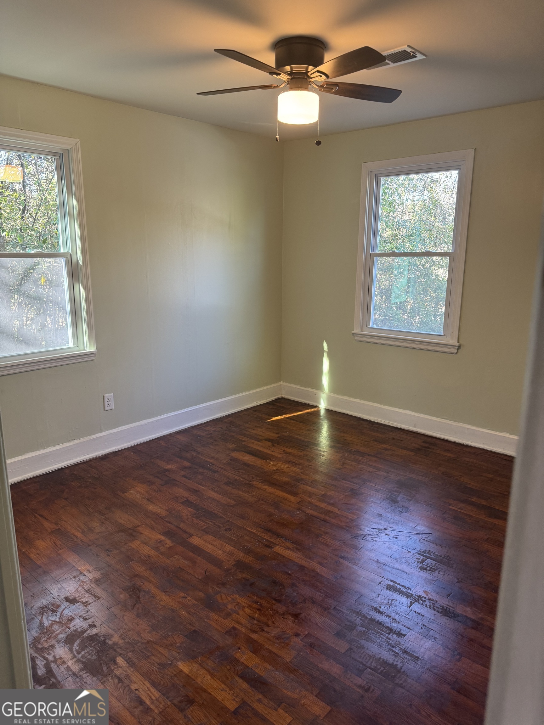 906 Central Avenue Dublin, GA 31021 - Photo 13 of 15 an empty room with wooden floor chandelier fan and windows