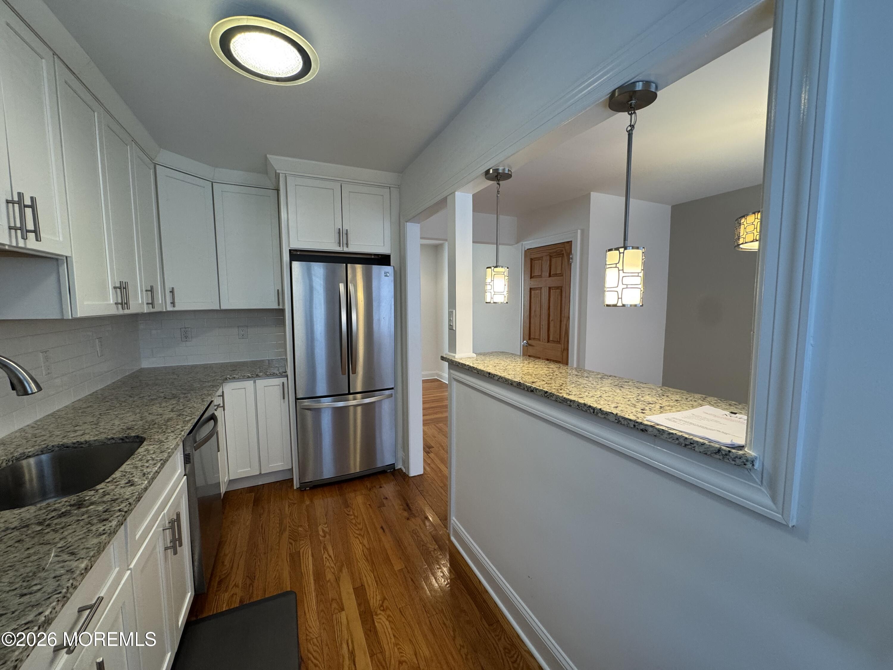 283 Spring Street, Unit 5B Red Bank, NJ 07701 - Photo 11 of 18 a kitchen with stainless steel appliances granite countertop a refrigerator a sink dishwasher a stove and white countertops with wooden floor