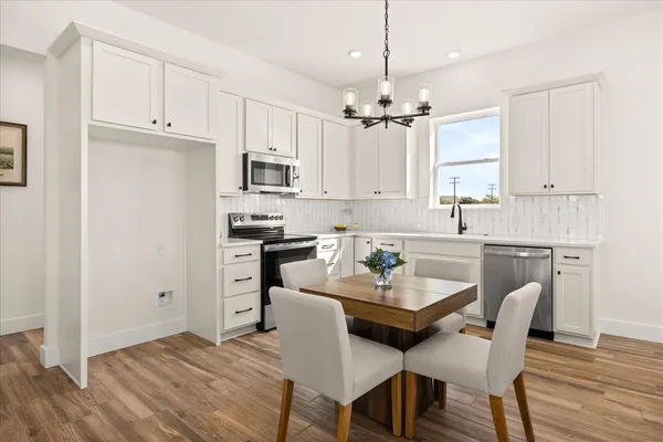 a kitchen with stainless steel appliances a white refrigerator a stove a sink dishwasher and white cabinets with wooden floor