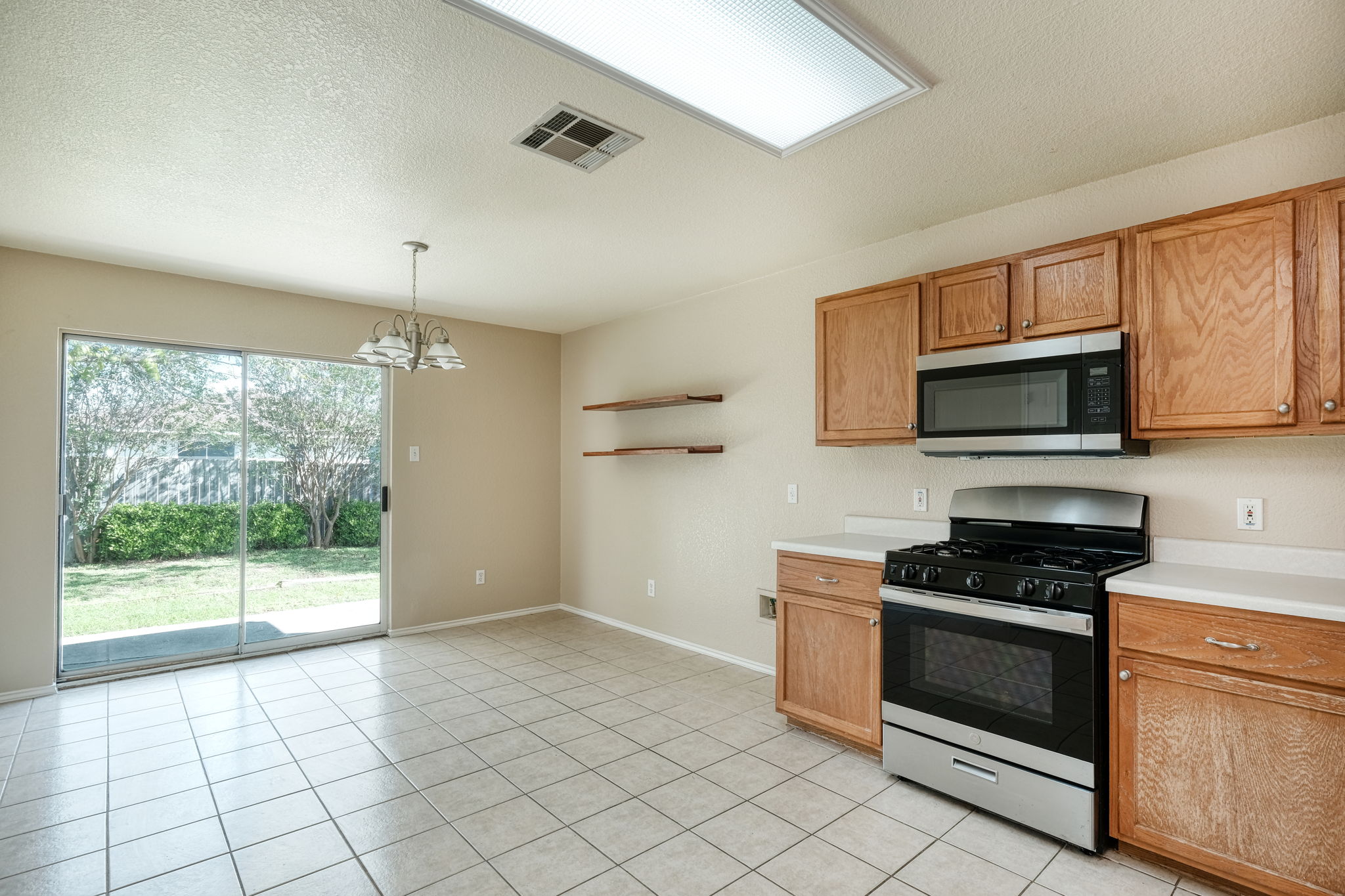 124 Hunter Rex Way Kyle, TX 78640 - Photo 4 of 14 Kitchen and dining area featuring tile flooring, light wood cabinetry, stainless steel range with overhead microwave, and sliding glass door access to the outdoor space