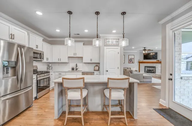 a kitchen with stainless steel appliances kitchen island granite countertop a dining table chairs and a refrigerator