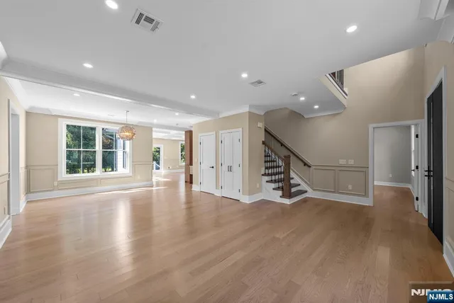 a view of an empty room with wooden floor stairs and a living room