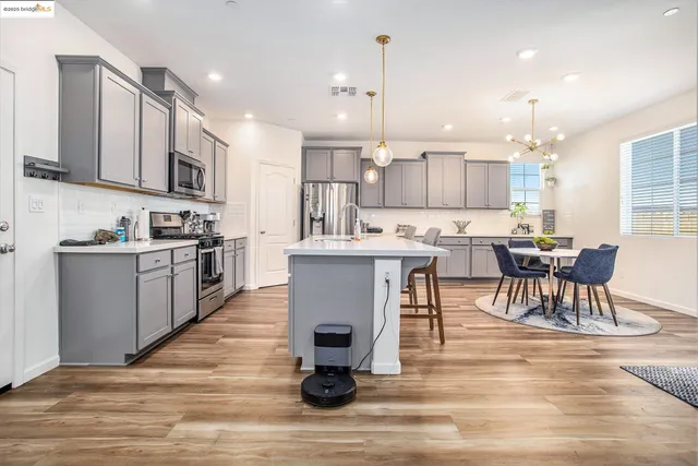 a kitchen with stainless steel appliances kitchen island granite countertop a stove a sink a refrigerator and white cabinets with wooden floor