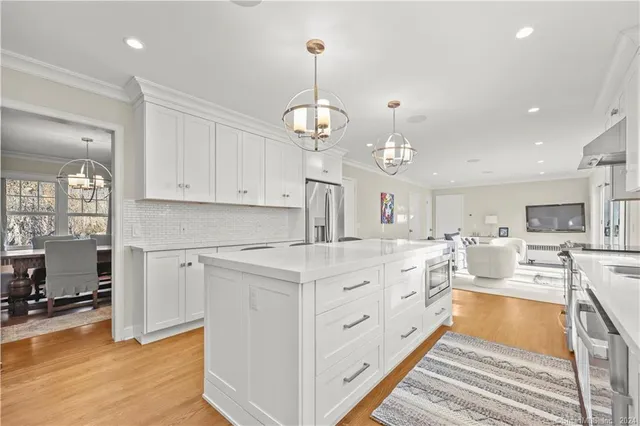 a large white kitchen with kitchen island a stove a sink dishwasher a dining table and chairs with wooden floor