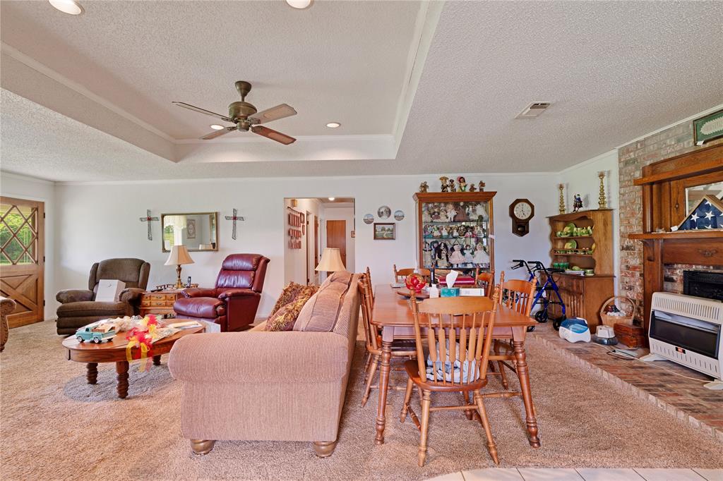1355 County Road 33100 Sumner, TX 75486 - Photo 24 of 34 Living area featuring heating unit, a textured ceiling, a ceiling fan, a tray ceiling, and a brick fireplace