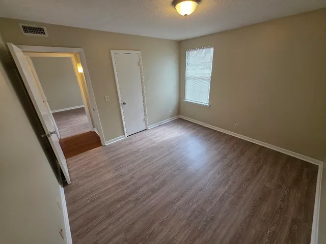 a view of an empty room with wooden floor and a window