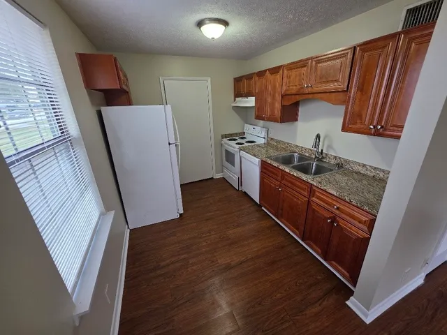 a kitchen with granite countertop wooden cabinets a sink a stove a refrigerator and wooden floor