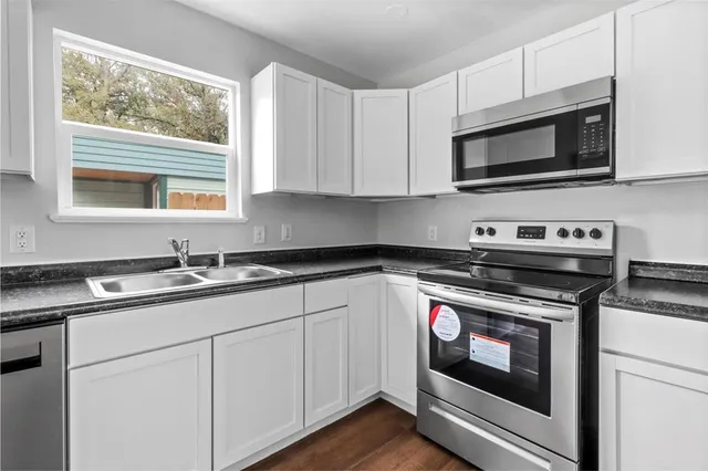 a kitchen with wooden floors white cabinets a sink and appliances