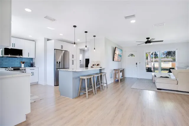 a kitchen with stainless steel appliances kitchen island granite countertop a refrigerator a stove top oven a sink dishwasher and white cabinets with wooden floor