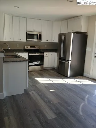 a kitchen with granite countertop a refrigerator a sink a stove a microwave and wooden floor