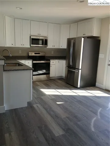 a kitchen with granite countertop a refrigerator a sink a stove a microwave and wooden floor