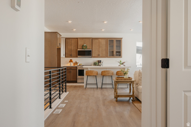 4595 North Fallow Way, Unit 511 Eagle Mountain, UT 84005 - Photo 27 of 32 Kitchen with a kitchen breakfast bar, light countertops, wood finish cabinetry, glass insert cabinets, and light wood-style flooring