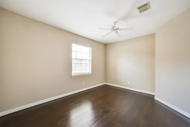 an empty room with wooden floor fan and windows