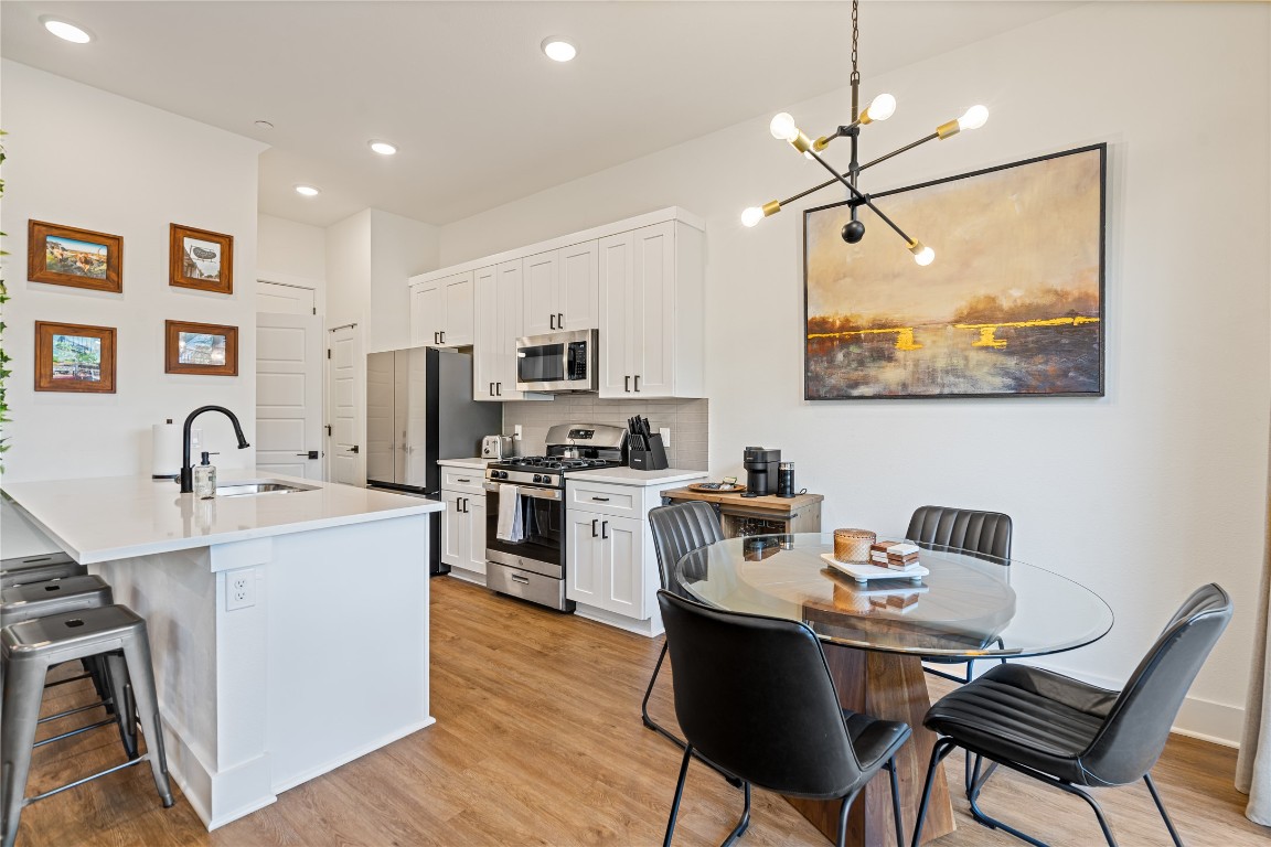 a kitchen with stainless steel appliances granite countertop a stove top oven a sink a dining table and chairs with wooden floor