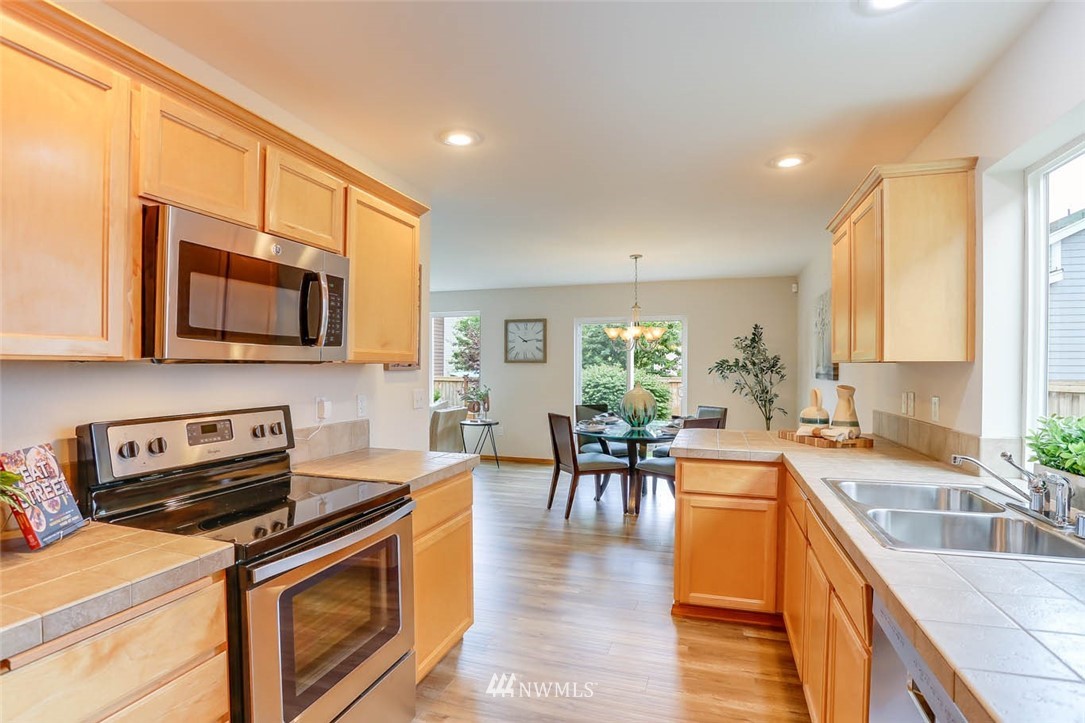 6731 Southeast 3rd Street Renton, WA 98059 - Photo 12 of 31 a kitchen with stainless steel appliances granite countertop a stove top oven a sink a dining table and chairs with wooden floor