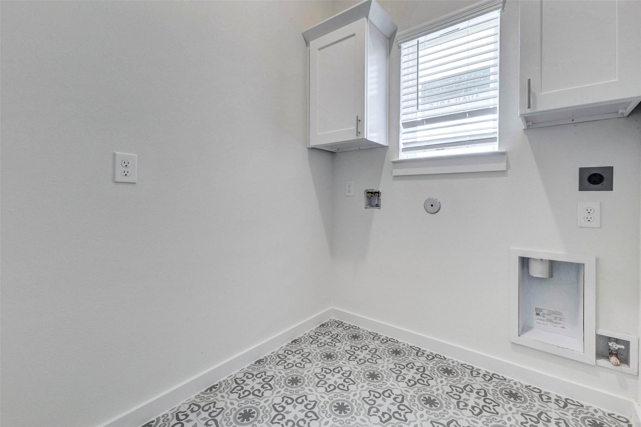 6475 Escondido Drive Rosharon, TX 77583 - Photo 28 of 32 The laundry room features patterned tile flooring, upper cabinetry, a window with blinds, and dedicated washer and dryer connections. The bright white walls and added storage create a clean, functional space designed to keep laundry tasks organized while adding a stylish touch with the decorative floor detail.