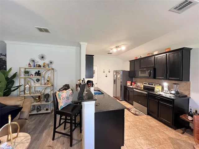 a kitchen with stainless steel appliances kitchen island granite countertop a sink dishwasher a stove a refrigerator a dining table and chairs with wooden floor