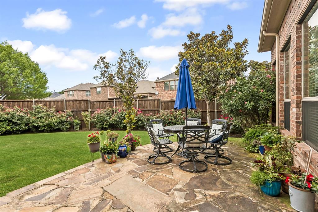 960 Remuda Road Frisco, TX 75033 - Photo 29 of 39 Expansive flagstone patio area featuring a dining set with a blue umbrella, surrounded by lush landscaping, a manicured lawn, and a privacy fence