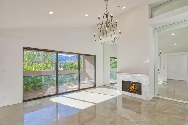 a view of a livingroom with a fireplace a chandelier and windows