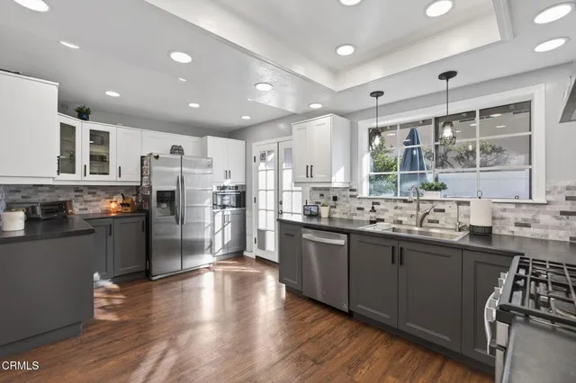 a kitchen with stainless steel appliances granite countertop a refrigerator a sink dishwasher a stove and a refrigerator with wooden floor