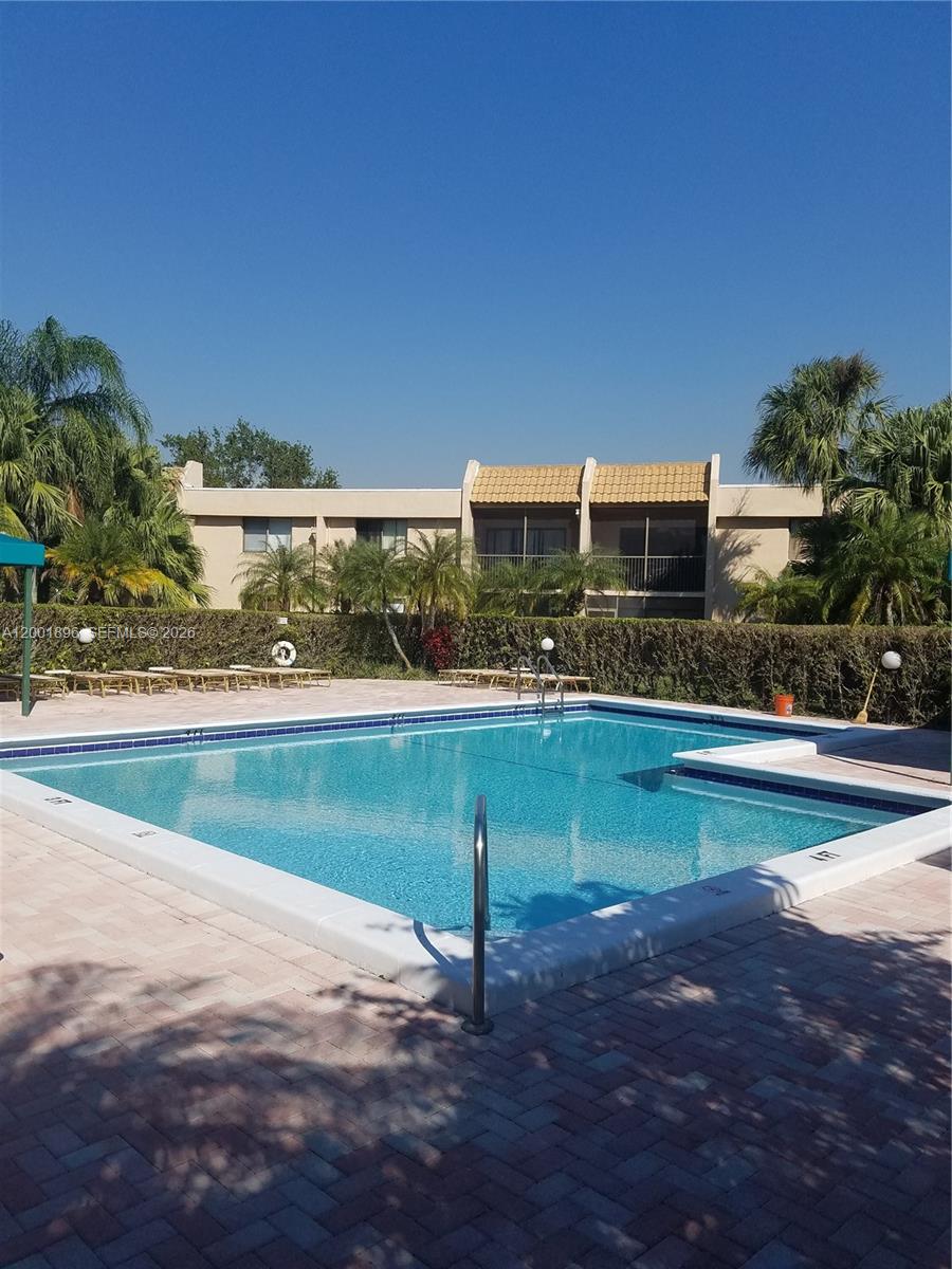 310 Racquet Club Road, Unit 204 Weston, FL 33326 - Photo 22 of 22 a view of a swimming pool with a lawn chairs under an umbrella