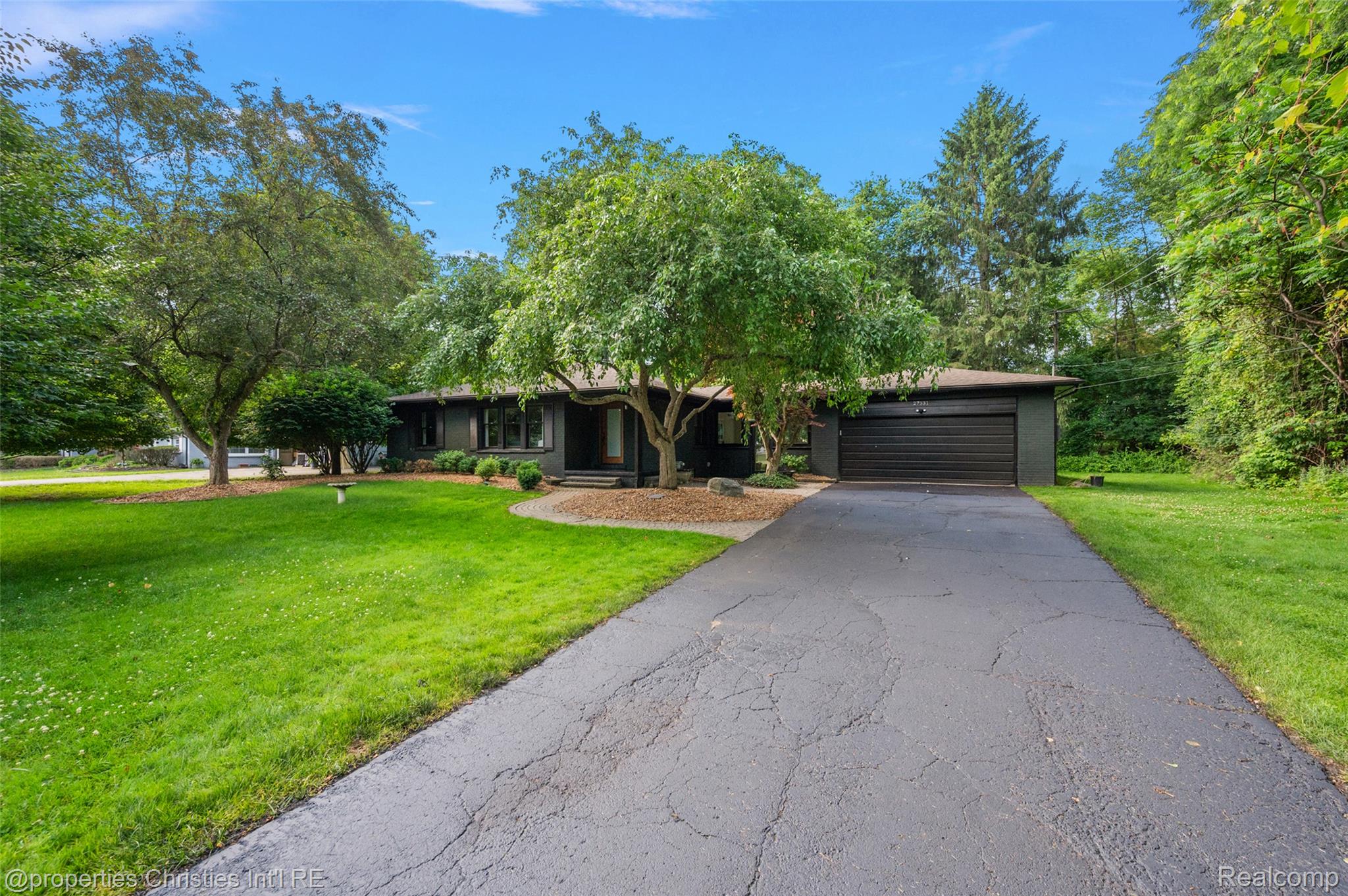 Single-story residence featuring a dark exterior, a prominent asphalt driveway, and an attached garage with a dark garage door