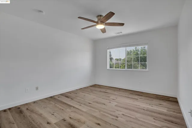 an empty room with wooden floor ceiling fan and windows