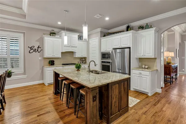 a kitchen with stainless steel appliances granite countertop a refrigerator a stove top oven a sink dishwasher and white cabinets with wooden floor
