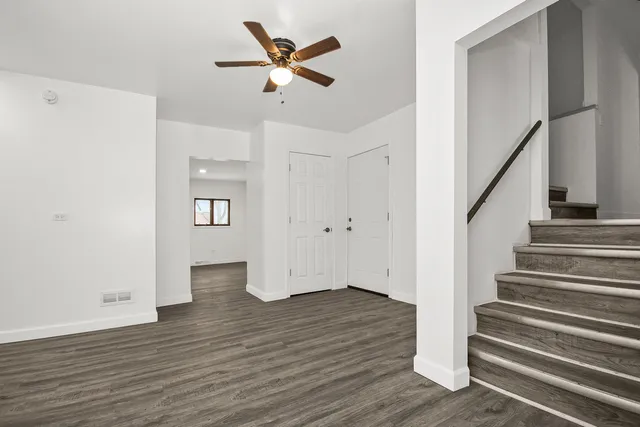 a view of an empty room with wooden floor and a ceiling fan
