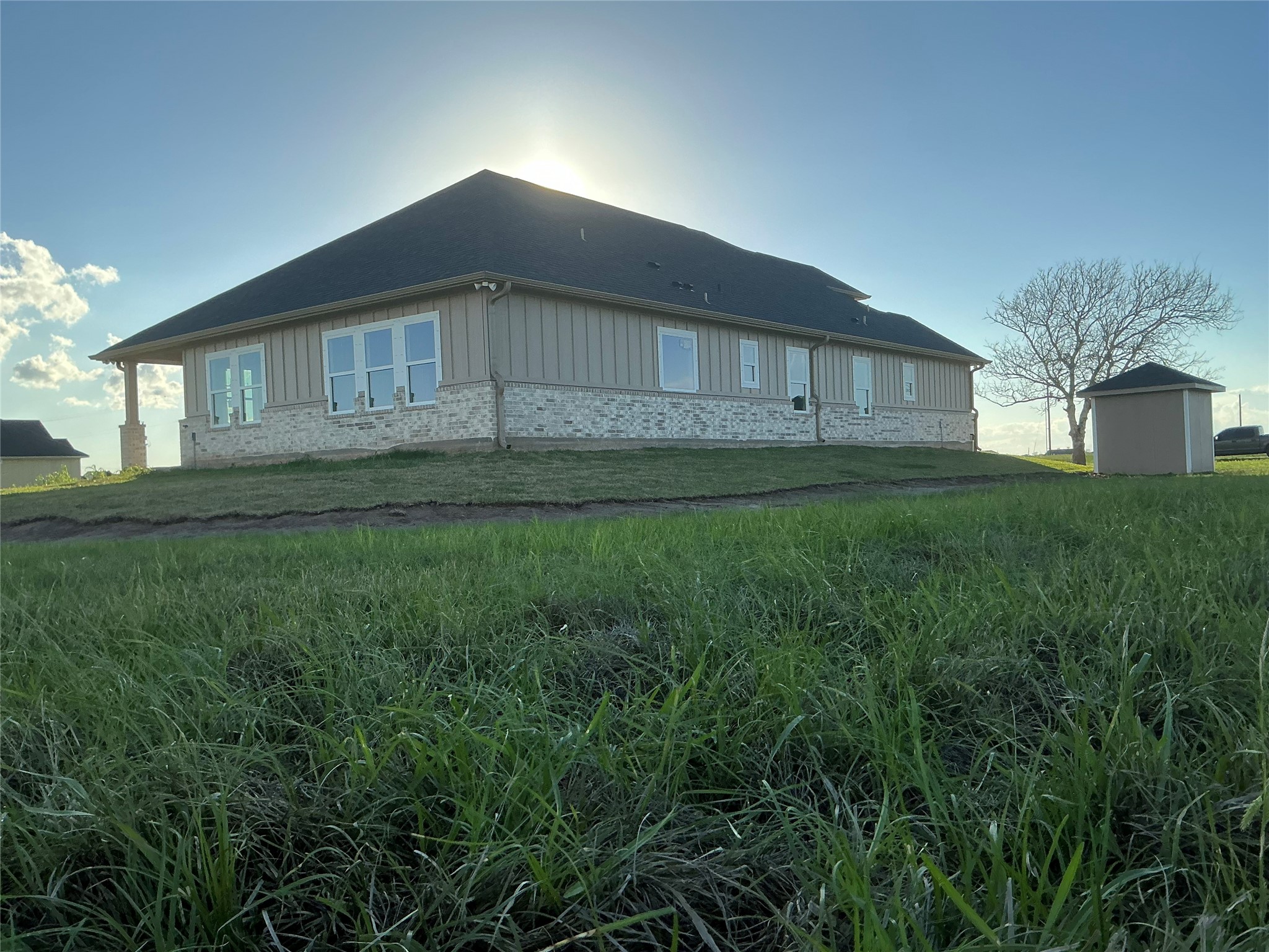 471 Buffalo Trail Angleton, TX 77515 - Photo 33 of 35 A single-story home with a modern design, featuring a combination of brick and siding. It has a sloped roof and large windows, surrounded by a spacious, grassy yard. The setting is open and sunny, creating a welcoming atmosphere.