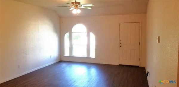 an empty room with wooden floor chandelier fan and windows