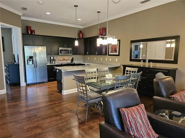 a kitchen with stainless steel appliances kitchen island granite countertop a refrigerator a stove a microwave oven a dining table and chairs with wooden floor
