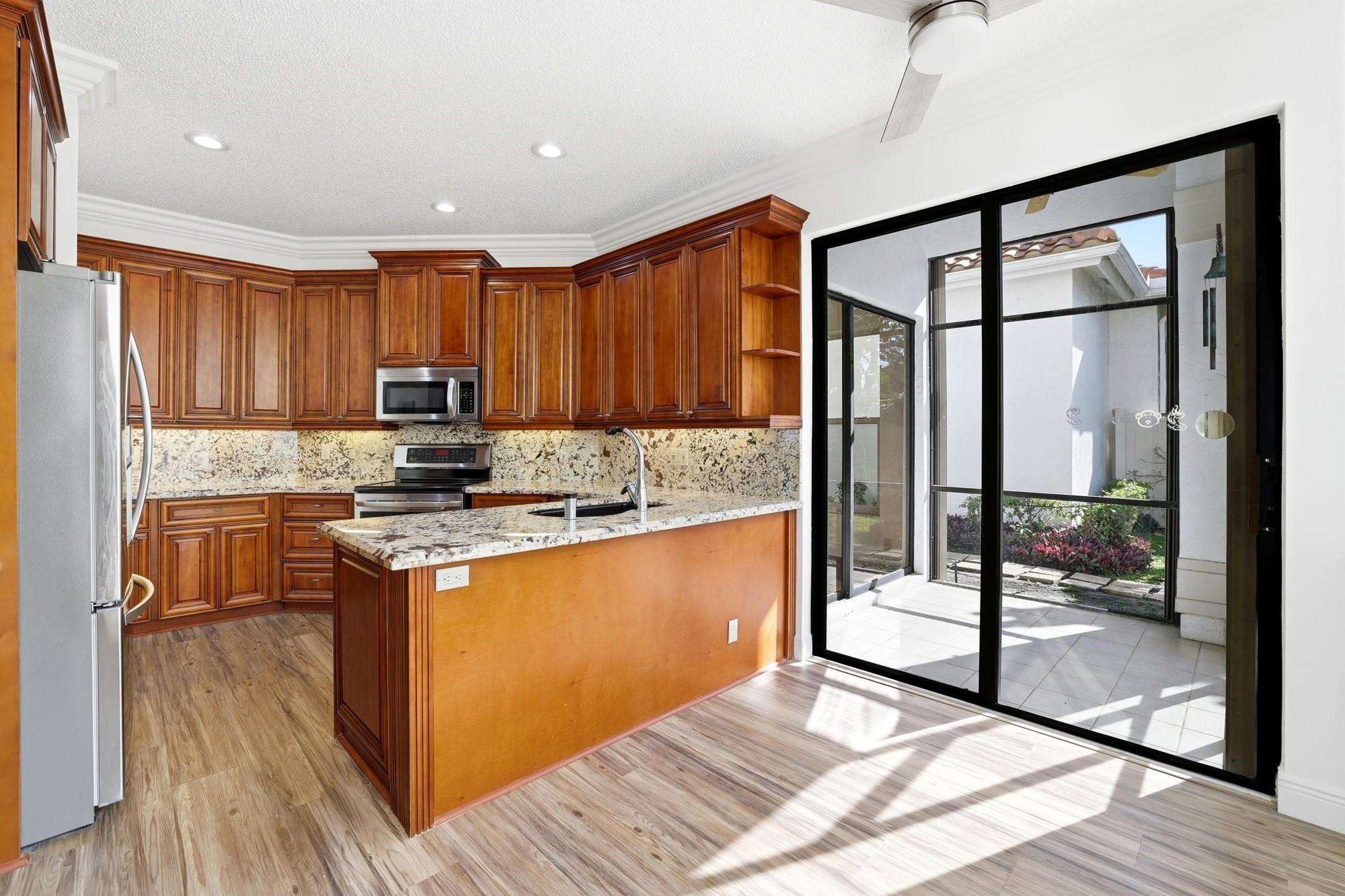 2498 Northwest 63rd Street Boca Raton, FL 33496 - Photo 11 of 39 a kitchen with kitchen island granite countertop wooden cabinets a sink and a stove