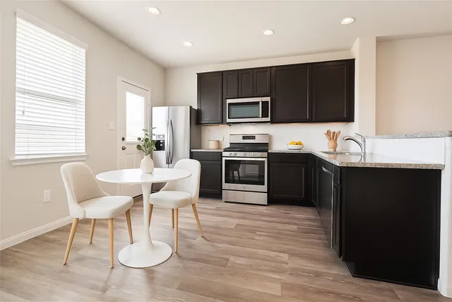 a kitchen with stainless steel appliances granite countertop a sink dishwasher a stove a refrigerator and a dining table with wooden floor